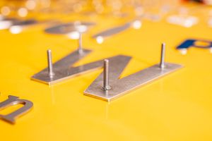 Metallbuchstaben - Bolzenbefestigung Metallbuchstaben aus Edelstahl - Befestigung mit Abstandshaltern auf Holzplatte