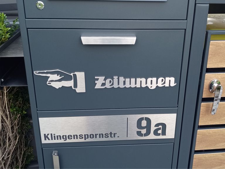 Gebürstetes Edelstahlschild mit Fingerzeig und dem Wort Zeitungen an einem Briefkasten