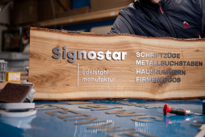Signostar Edelstahlmanufaktur - Firmenlogos aus Edelstahl - Metallbuchstaben auf Holzbrett