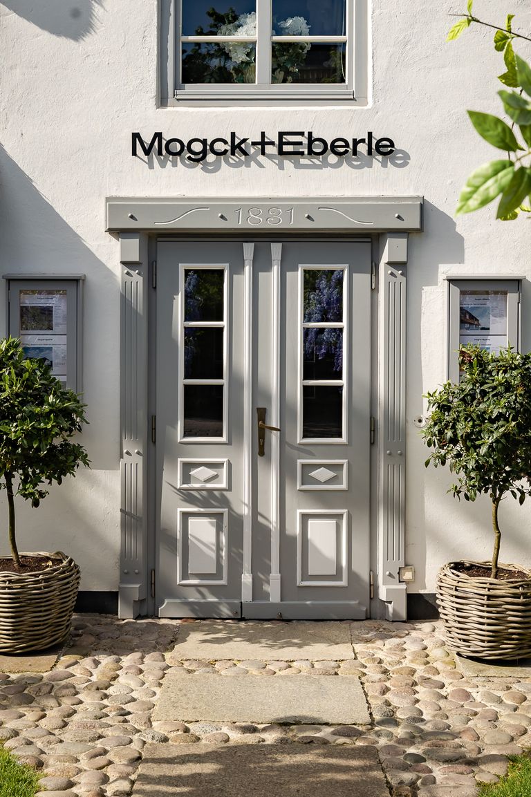 Schwarzes Firmenlogo Mogck + Eberle aus Edelstahl über historischer Eingangstür