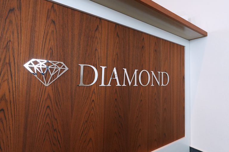 Schriftzug Diamond mit poliertem Edelstahl-Logo auf Holzfront an einem Empfangstresen