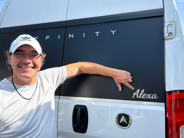 Mann zeigt auf den Namensschriftzug Alexa aus Edelstahl an einem schwarzen Fahrzeugheck