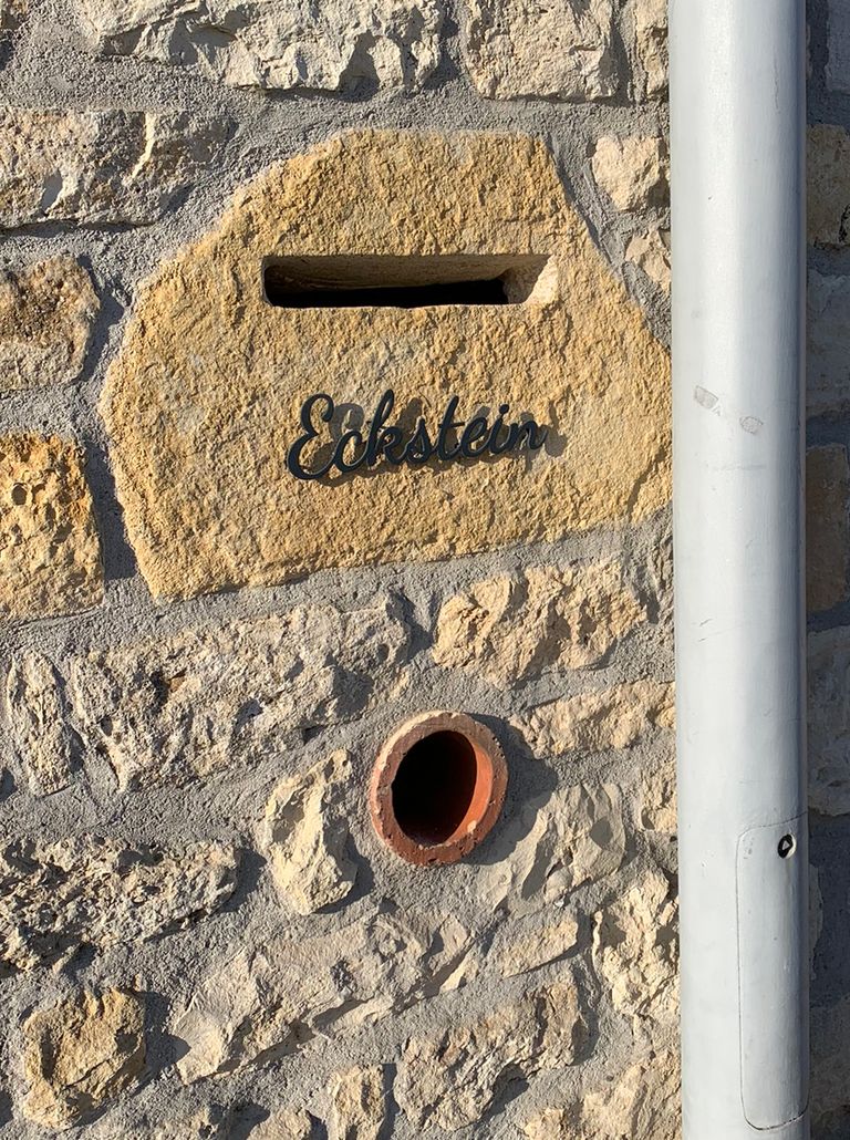 Schriftzug Eckstein in schwarzem Edelstahl auf hellem Natursteinmauerwerk