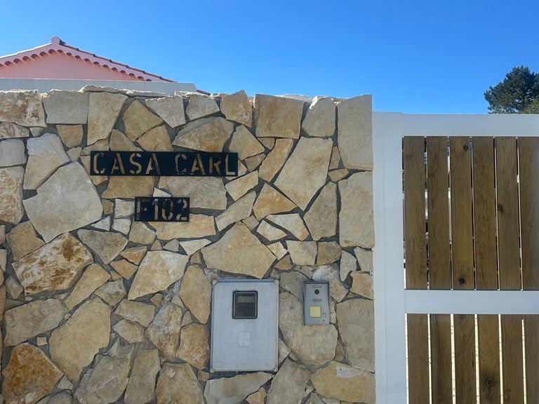 Schwarzes Schild Casa Carl 102 aus Edelstahl an Natursteinmauer mit Holz-Gartentor