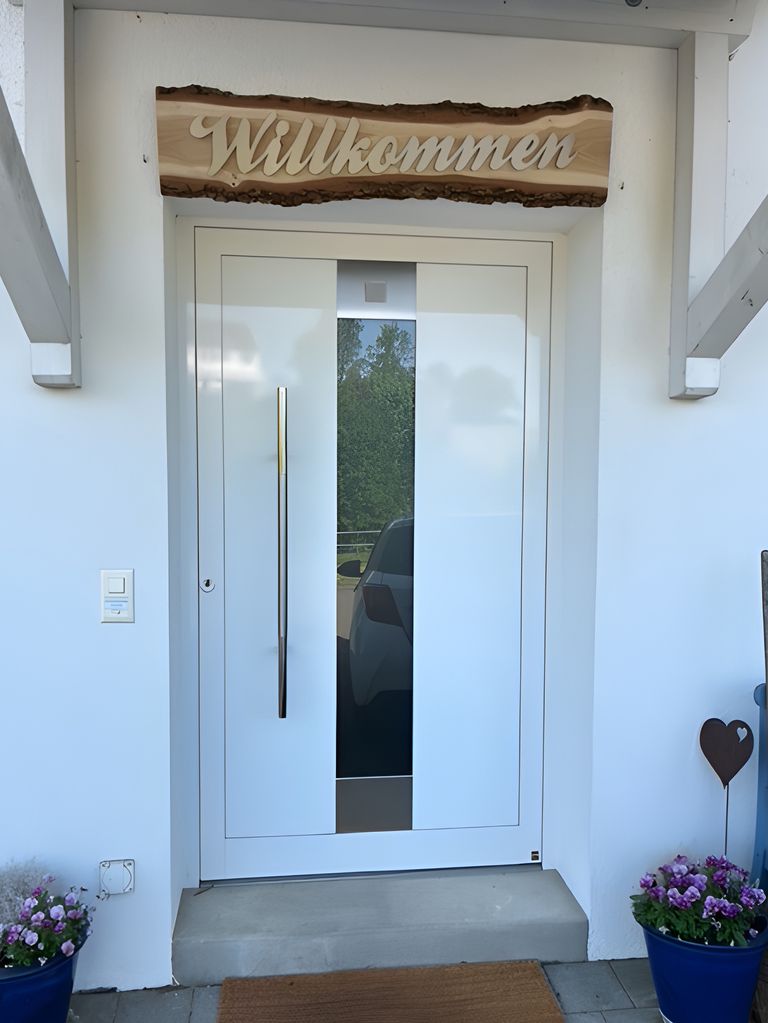 Willkommensschild aus gebürstetem Edelstahl auf Holzbrett über weißer Eingangstür