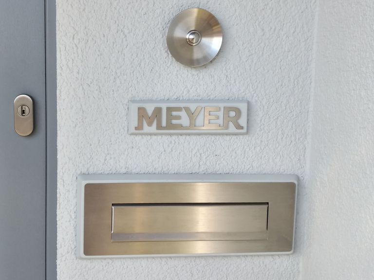 Hauswand mit Klingel und graviertem Edelstahlschild Meyer über dem Briefkasten