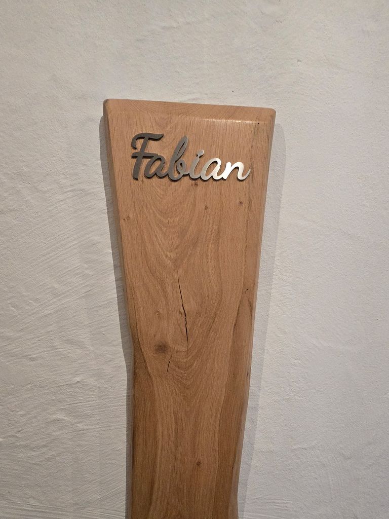 Schriftzug Fabian aus Edelstahl auf einem hölzernen Wachstumsbrett an der Wand