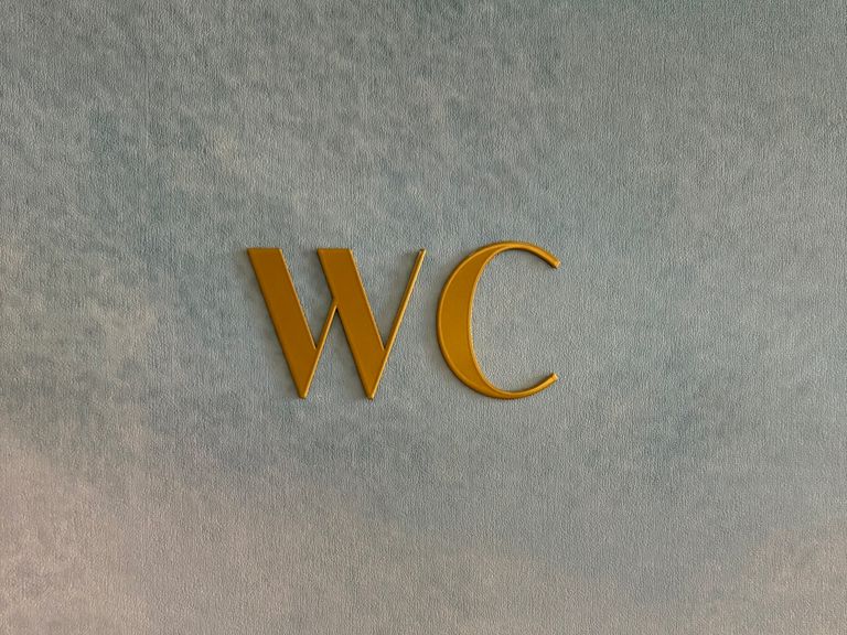 Schriftzug WC aus goldfarbenem Edelstahl auf strukturierter Wand